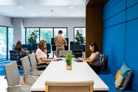 Apt CoWork Community Workspace at Sugarmont Apartments in SLC Modern coworking space with bright interiors, featuring professionals engaged in work at a long white table, surrounded by large windows and vibrant blue accents at Apt CoWork at Sugarmont Apartments in SLC