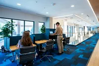 Apt CoWork Semi Private Sit Stand Desks at Sugarmont Apartments in Salt Lake City Modern co-working space featuring stylish workstations, vibrant blue carpet, and large windows for natural light at Apt CoWork at Sugarmont Apartments in Sugarhouse