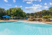 Inviting outdoor swimming pool with cascading waterfall and cozy cabanas, set against lush trees and a vibrant sky at Enclave on Golden Triangle in Forth Worth Texas