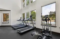 Modern fitness center with large windows showcasing lush greenery and pool views, featuring state-of-the-art treadmills and elliptical machine for an energizing workout experience at Enclave on Golden Triangle Apartments in Fort Worth Texas