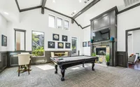 Luxurious game room featuring a sleek pool table, elegant seating area, and a cozy fireplace under high ceilings at Enclave on Golden Triangle Apartments in Fort Worth Texas