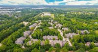 Scenic aerial view of a lush, green residential community surrounded by trees, featuring modern houses with spacious yards and a bright blue sky above  at Raveneaux Apartments in Houston Texas