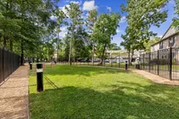 Charming green pet park and outdoor space with a walking path, perfect for relaxation and leisure in a peaceful apartment community  at Raveneaux Apartments in Houston Texas