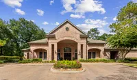 Raveneaux Apartmetns brick building with elegant arches surrounded by lush greenery and a vibrant garden under a bright blue sky in Houston Texas