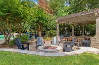 Inviting outdoor space featuring a cozy fire pit surrounded by stylish seating, lush greenery, and a charming pergola perfect for gatherings at Raveneaux Apartments in Houston