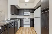 Modern kitchen with elegant dark wood cabinets, spacious countertops, and essential white appliances on sleek hardwood flooring at Raveneaux Apartments in Houston TX