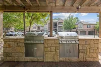Charming outdoor BBQ area with stainless steel grills under a rustic pergola, perfect for social gatherings at Raveneaux Apartments in Houston