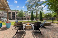 Charming outdoor patio with cozy fire pit, surrounded by Adirondack chairs and lush greenery, perfect for relaxation and social gatherings at a beautiful apartment community at Raveneaux Apartments in Houston TX