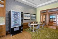 The Marq Highland Apartments Park Apt CoWork Snack Station Westchase Tampa, FL Coworking office with snack machine featuring a community workspace seating with round tables, and artistic wall decor for a welcoming atmosphere at Apt CoWork at The Marq Highland Park in Westchase Tampa Florida