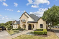Charming stone apartments with elegant arched entrance, surrounded by lush greenery under a bright blue sky at Stonebriar at Frisco Apartments in Frisco Texas