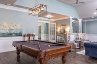 Elegant and inviting clubroom at The Stratford at Hillcrest Towne Center Apartments featuring a stylish billiard table, modern lighting, and comfortable seating, perfect for entertaining and relaxation.