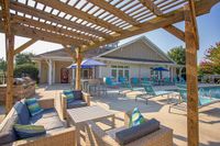 Charming outdoor patio at The Stratford at Hillcrest Towne Center Apartments with wicker furniture, vibrant blue loungers, and a sunlit pergola beside a refreshing pool.