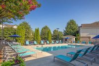 Elegant swimming pool area at The Stratford at Hillcrest Towne Center Apartments with turquoise loungers, vibrant greenery, and a cozy seating pavilion under a clear blue sky.