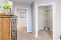 Inviting apartment interior featuring a cozy hallway, elegant wooden dresser with decorative accents, and a spacious open closet with plush carpet flooring, perfect for stylish living at The Stratford at Hillcrest Towne Center Apartments.