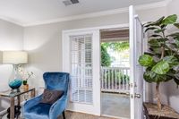 Inviting living space at The Stratford at Hillcrest Towne Center Apartments with elegant blue armchair, stylish lamp, and private patio access through glass doors, complemented by greenery for a serene ambiance.