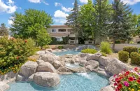 Charming apartment complex with a picturesque rock waterfall feature surrounded by vibrant flowers and lush greenery at Pavilions Apartments in Albuquerque.