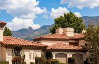Charming homes with terracotta roofs set against a stunning mountain backdrop, surrounded by lush greenery and blue skies at Pavilions Apartments in Albuquerque.