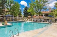 Inviting outdoor pool area with sun loungers, vibrant umbrellas, and lush greenery, perfect for relaxation and leisure at Pavilions Apartments in Albuquerque.