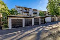 Charming apartment exterior with individual garages and lush greenery under a bright blue sky at Scott Mountain Apartments in Portland OR.