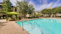 Luxurious apartment complex showcasing a sparkling swimming pool surrounded by elegant stone architecture and lush greenery.