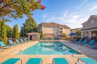Inviting outdoor pool area with vibrant blue lounge chairs, surrounded by lush greenery and charming apartment buildings at Stratford at Hillcrest Apartments in Winston-Salem.