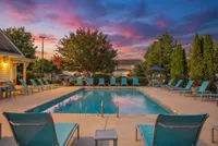 Inviting apartment complex pool area with vibrant lounge chairs, surrounded by lush greenery and a breathtaking sunset sky at Stratford at Hillcrest Apartments at Dusk