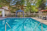 Inviting swimming pool area with elegant lounge chairs, a stylish striped cabana, and lush greenery creating a serene oasis.