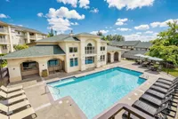 Elegant apartment complex featuring a sparkling blue swimming pool, luxurious loungers, and scenic surroundings under a bright blue sky.