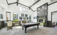Luxurious game room featuring a sleek pool table, elegant seating area, and a cozy fireplace under high ceilings at Enclave on Golden Triangle Apartments in Fort Worth Texas