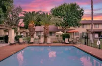 Inviting apartment complex in Yuma with a serene pool area, lush palm trees, and cozy lounge seating at sunset.