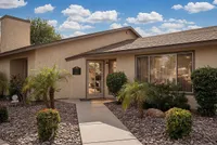Charming leasing office at Camelot Apartments with a landscaped entrance, featuring lush greenery and a welcoming pathway, under a bright blue sky in Yuma, AZ.