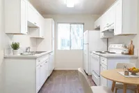 Bright and inviting kitchen at Camelot Apartments with modern white cabinets, sleek countertops, and warm wood flooring, perfect for culinary adventures.