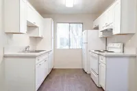 Bright modern kitchen at Camelot Apartments with white cabinetry, sleek countertops, and natural light through a large window.