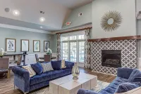 Elegant clubroom at The Stratford at Hillcrest Towne Center Apartments with plush blue sofas, geometric fireplace, modern decor, and large windows offering abundant natural light.