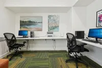 Modern home office with dual workstations featuring sleek computers, ergonomic chairs, vibrant artwork, and patterned carpet.