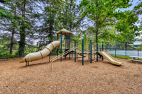 Charming playground with slides and climbing structures surrounded by lush green trees, perfect for family activities and outdoor fun.