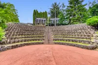 Charming outdoor amphitheater with tiered stone seating surrounded by lush greenery, perfect for open-air events.