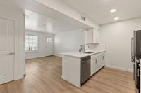 Bright open kitchen with sleek white cabinets, elegant countertops, and modern appliances, showcasing a spacious open floor plan and natural light.