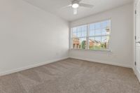 Bright, cozy bedroom featuring plush carpet, a ceiling fan, and large windows with a charming neighborhood view.