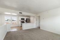 Bright open-concept living space with large windows, modern kitchen with stainless steel appliances, and plush carpeting.