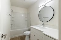 Modern bathroom featuring sleek white vanity, circular mirror, and pristine bathtub with neutral tones.