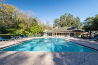 Inviting outdoor pool area surrounded by lounge chairs and lush greenery under a clear blue sky.