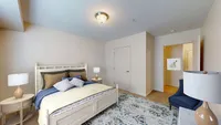 Inviting bedroom with a plush bed, elegant lamps, and a stylish blue accent chair, radiating comfort and tranquility.