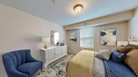 Charming bedroom with elegant decor featuring a plush blue armchair, stylish dresser, and cozy bedding accented by modern art.