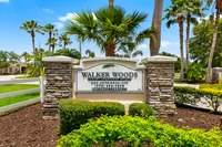 Inviting entry sign for Walker Woods Luxury Apartment Homes surrounded by lush greenery and palm trees under a clear blue sky.