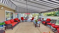 Charming outdoor patio featuring cozy red-cushioned seating, elegant striped awning, and delightful potted plants, perfect for relaxation and entertainment.
