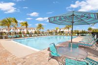 The pool area at our townhomes in Apopka, FL, featuring reclining chairs, palm trees, and a view of the townhomes.