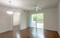 Bright living room with elegant wood floors, modern ceiling fan, and large sliding glass doors leading to a serene outdoor view.