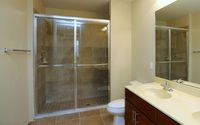 Bathroom with dual-sink vanity, glass-enclosed walk-in shower, tile flooring, and large mirror.