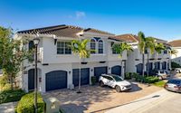 Charming Mediterranean-style townhomes with tile roofs, palm trees, and attached garages under a bright blue sky.